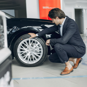 Man in suit inspecting car alloy wheel and tire in showroom