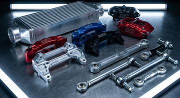 A dramatic close-up flat-lay of precision-machined billet aluminum Audi performance parts arranged on a dark brushed steel surface under sharp industrial lighting.