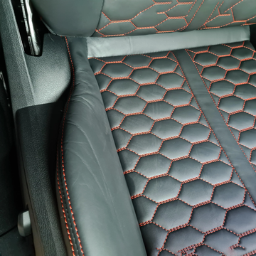 Black leather car seat with red hexagonal stitching and embossed pattern