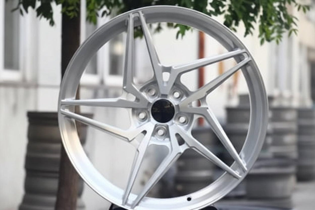 Silver multi-spoke alloy wheel for Audi, displayed outdoors with trees and buildings in background.