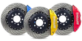 Set of three slotted and drilled performance brake rotors with red, yellow, and blue calipers