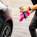 Person applying ceramic coating spray to black car wheel with pink microfiber towel