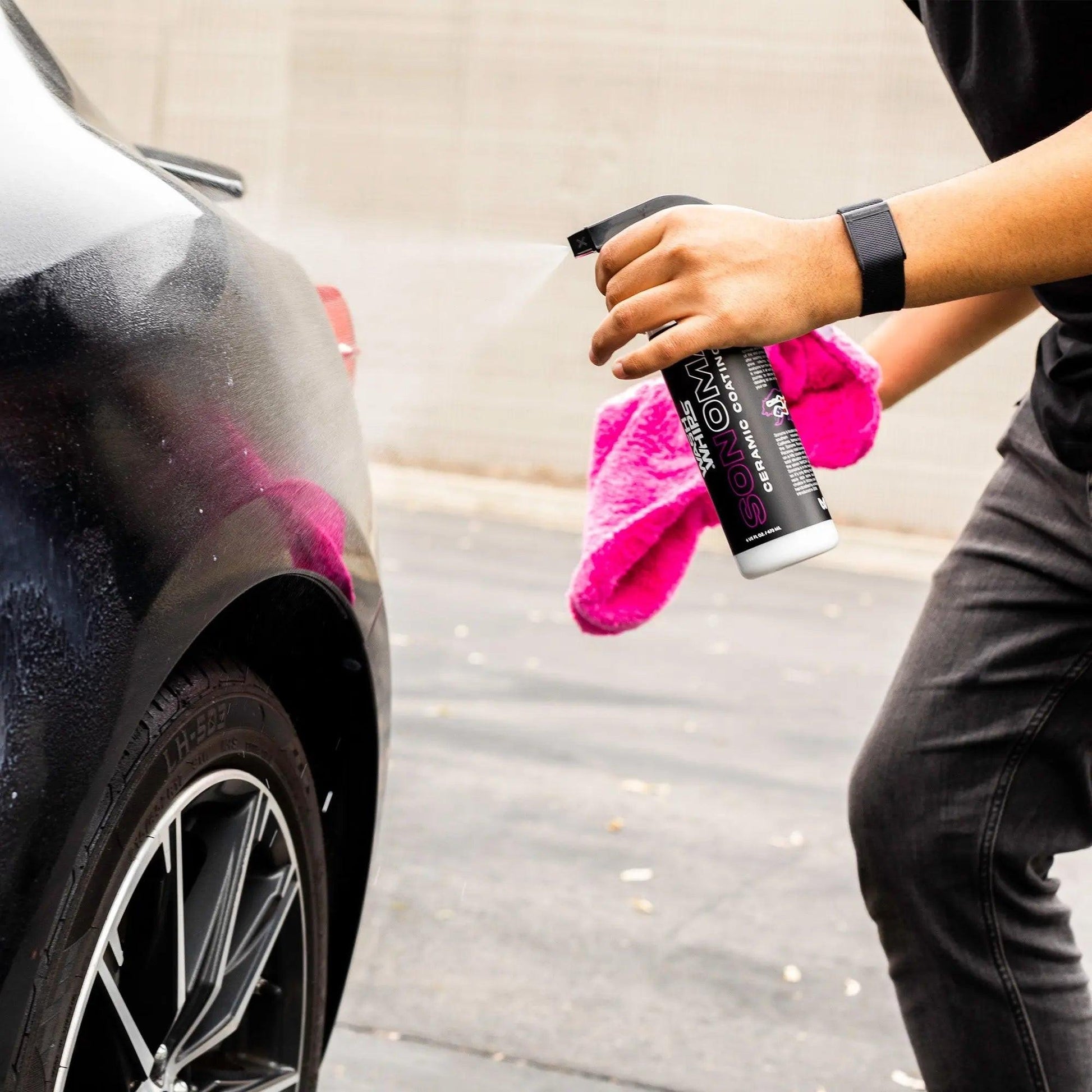 Person applying ceramic coating spray to black car wheel with pink microfiber towel