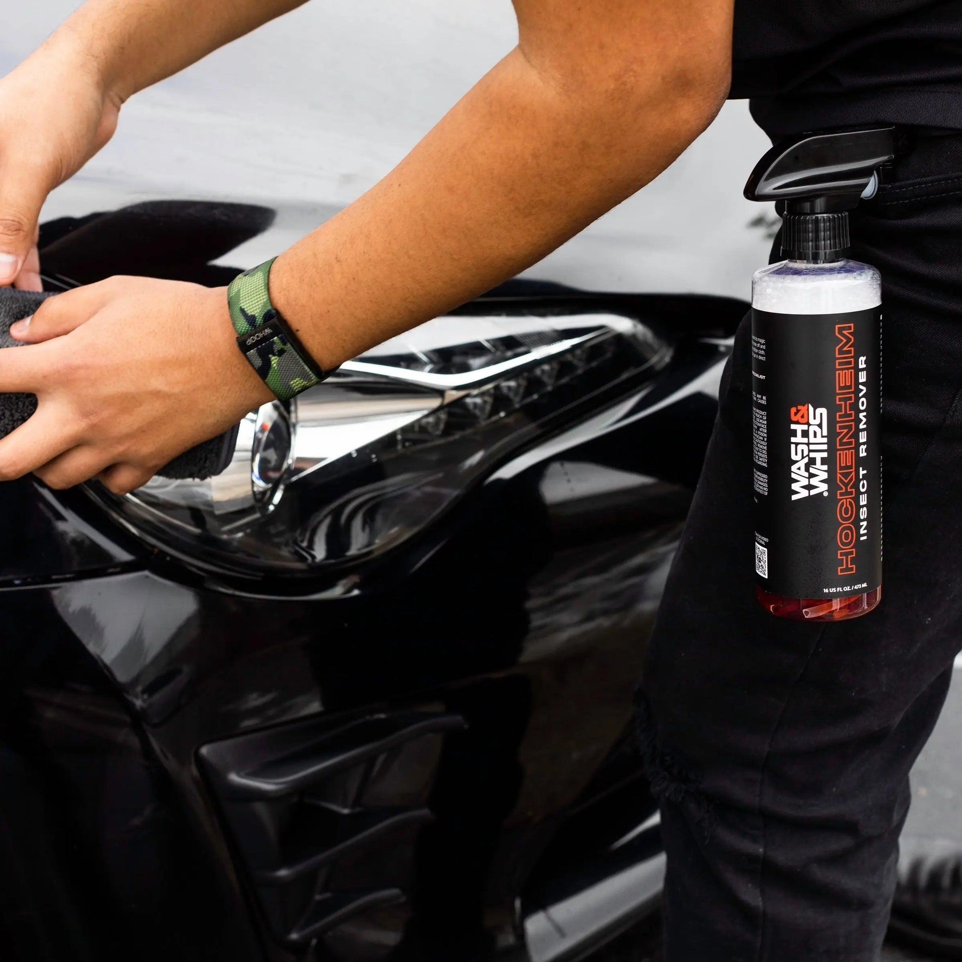 Hand cleaning black car headlight with Hockenheim insect remover spray clipped to belt