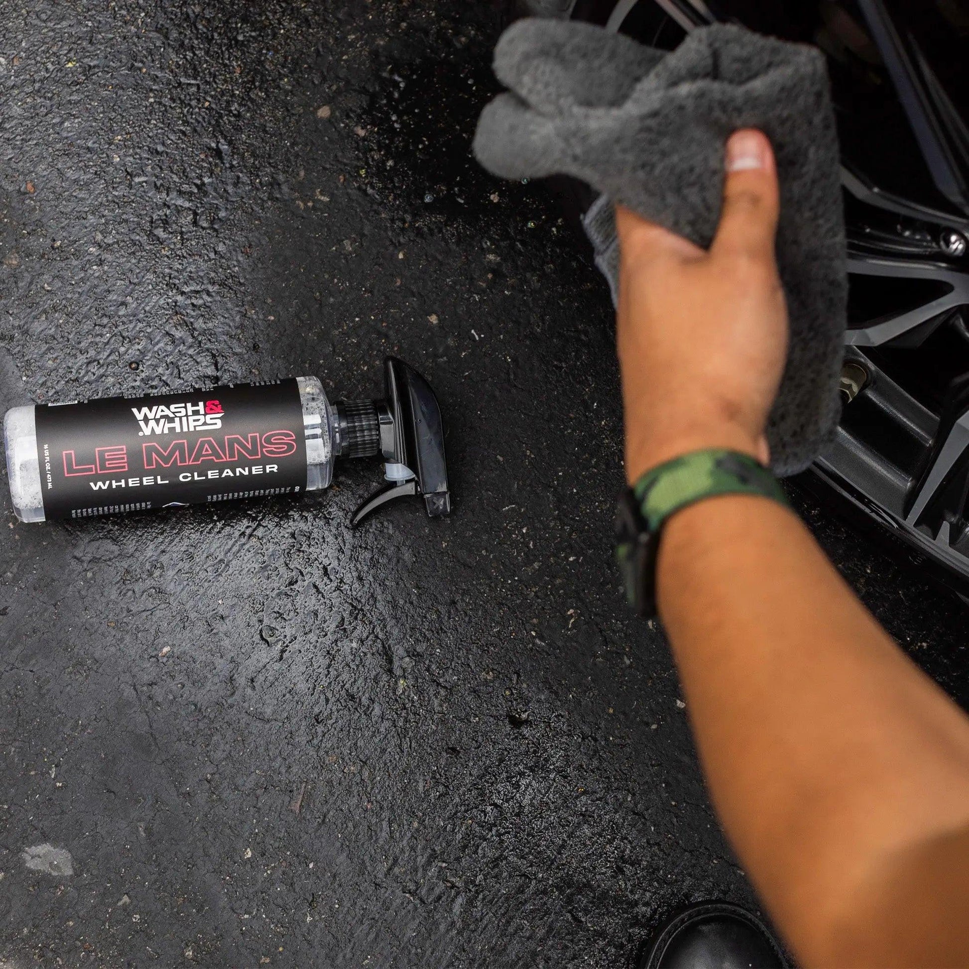 Car wheel cleaner spray bottle, microfiber glove, and alloy wheel on wet pavement