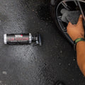Person cleaning car wheel with Wash & Whips Le Mans wheel cleaner spray on wet pavement