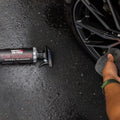 Person cleaning black alloy wheel with Wash Whips Le Mans wheel cleaner bottle on ground
