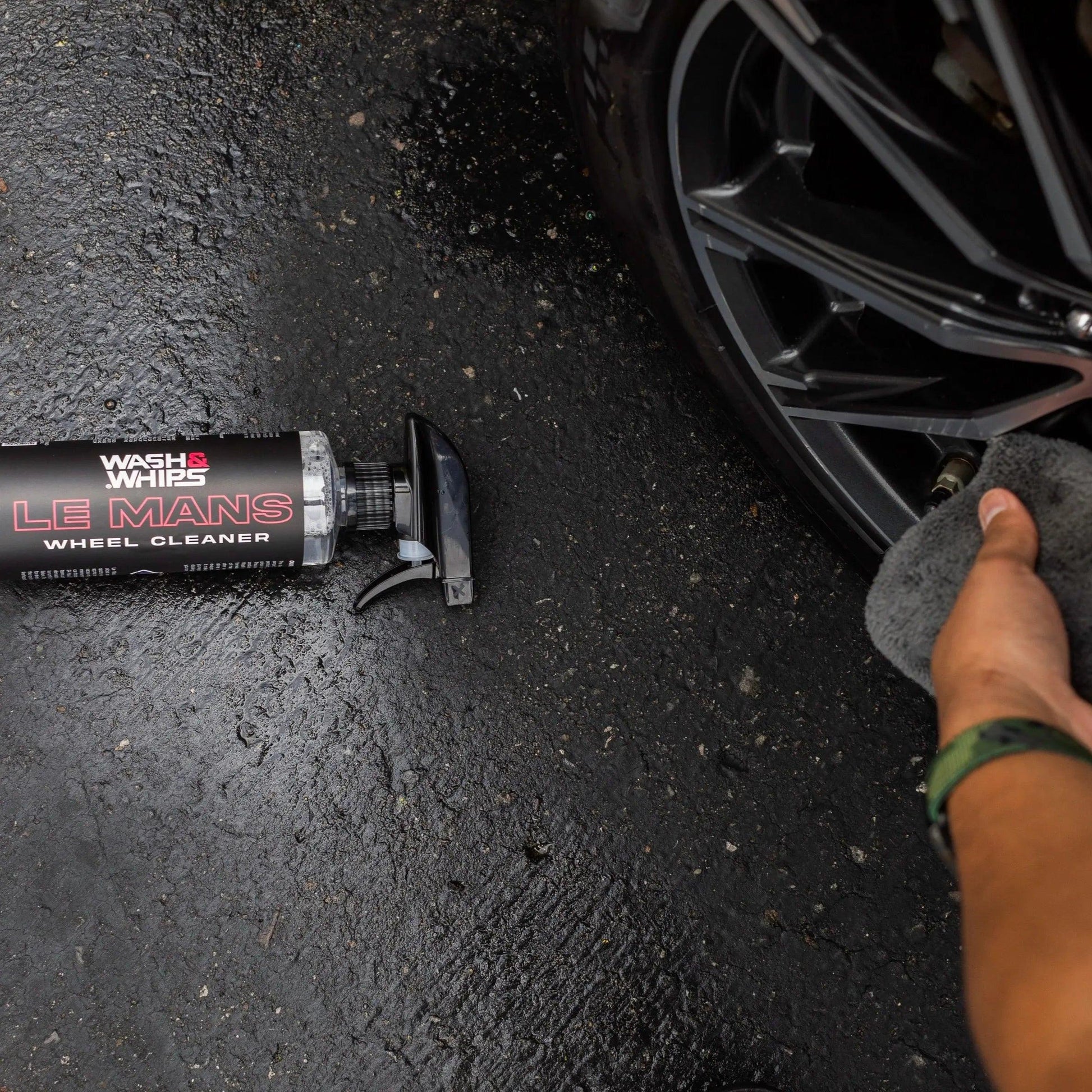 Person cleaning black alloy wheel with Wash Whips Le Mans wheel cleaner bottle on ground
