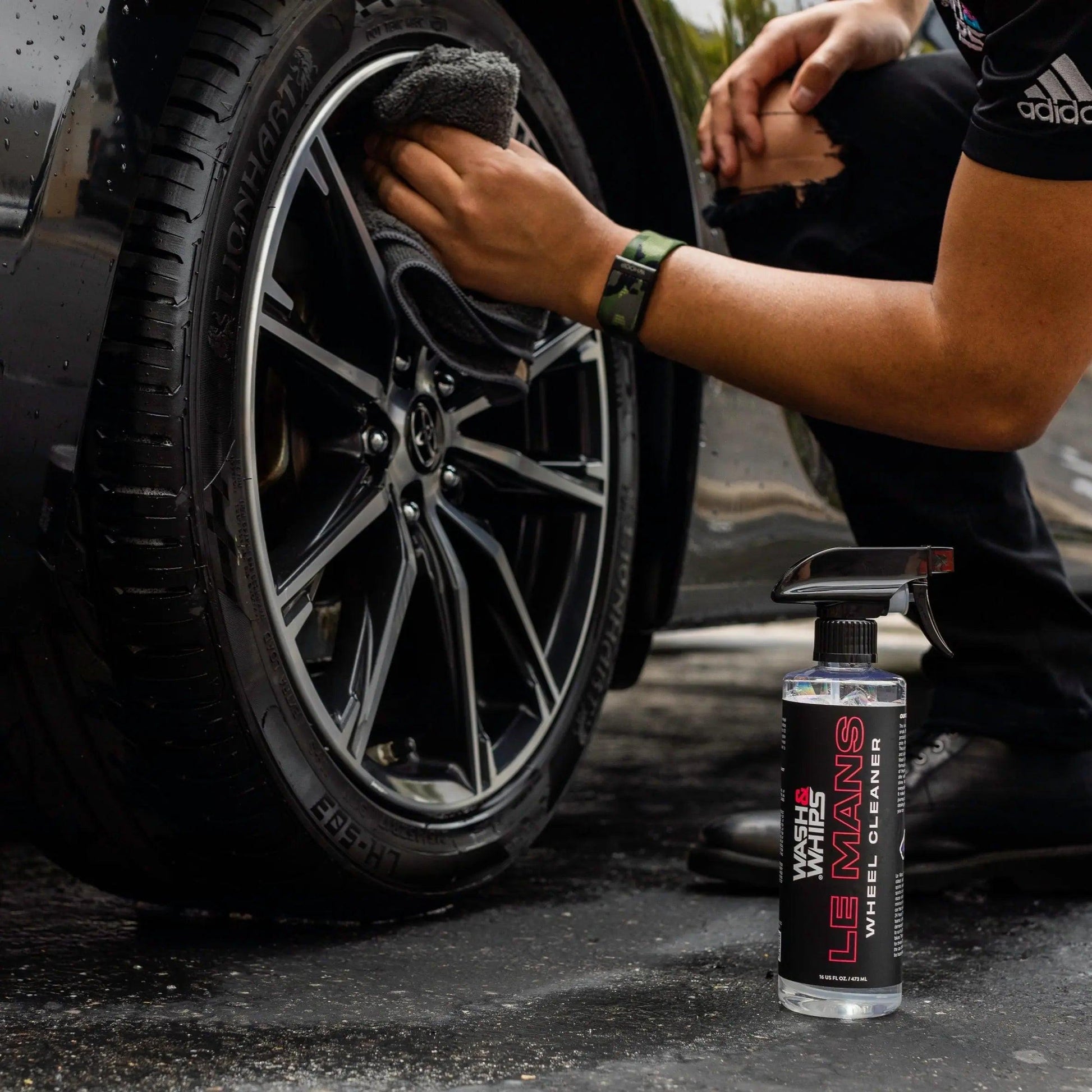 Person cleaning black Audi wheel with microfiber cloth, Le Mans wheel cleaner bottle nearby