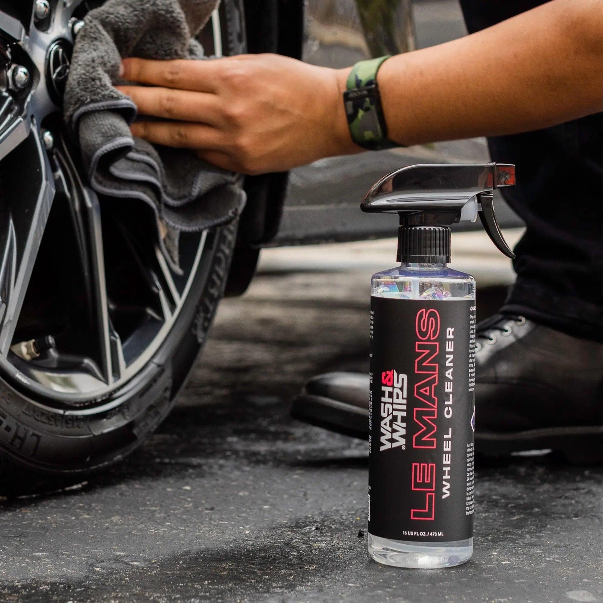 Person cleaning car wheel with microfiber towel and Le Mans wheel cleaner spray bottle