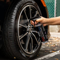 Hand spraying wheel cleaner on a black car alloy wheel and tire for shine and protection