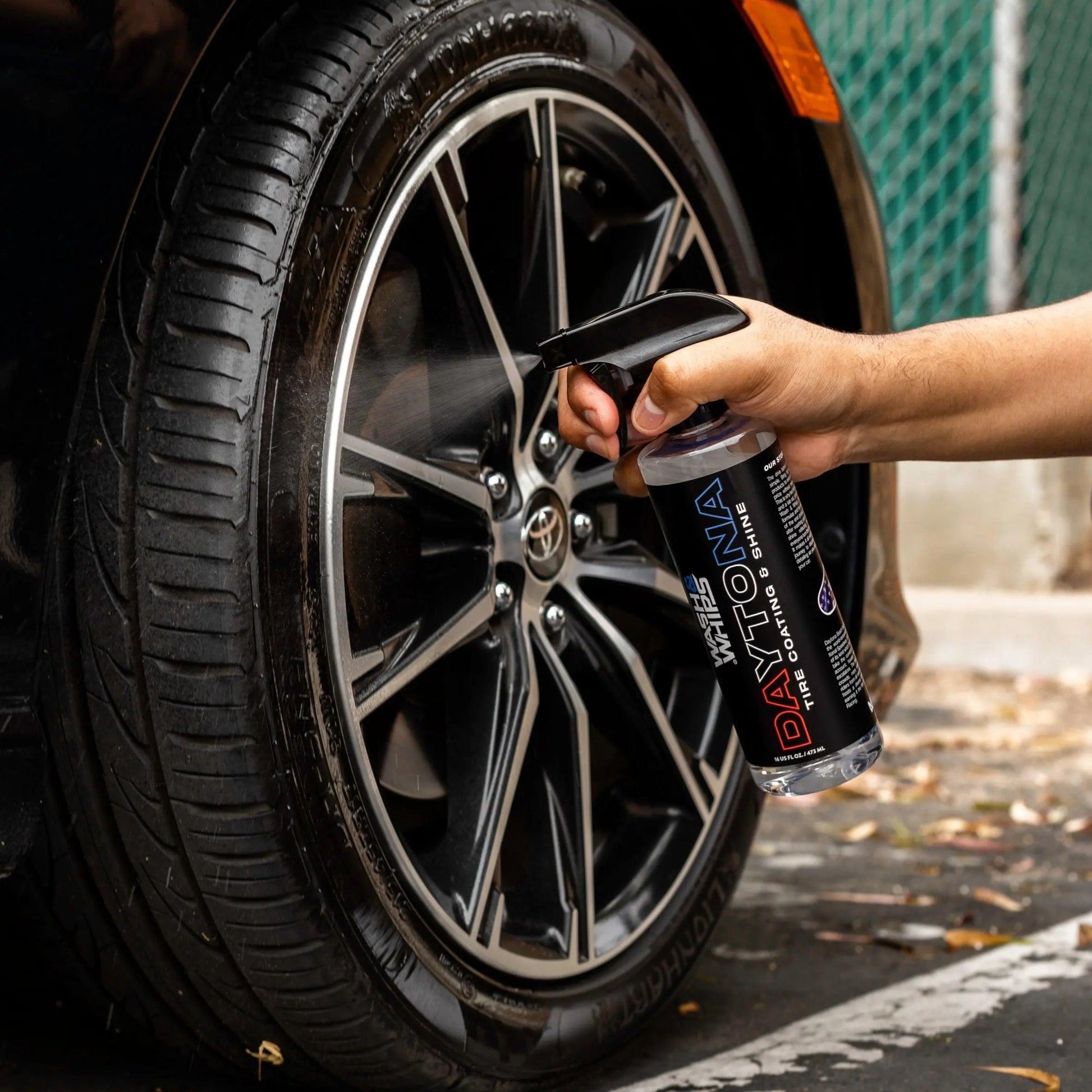 Hand spraying wheel cleaner on a black car alloy wheel and tire for shine and protection
