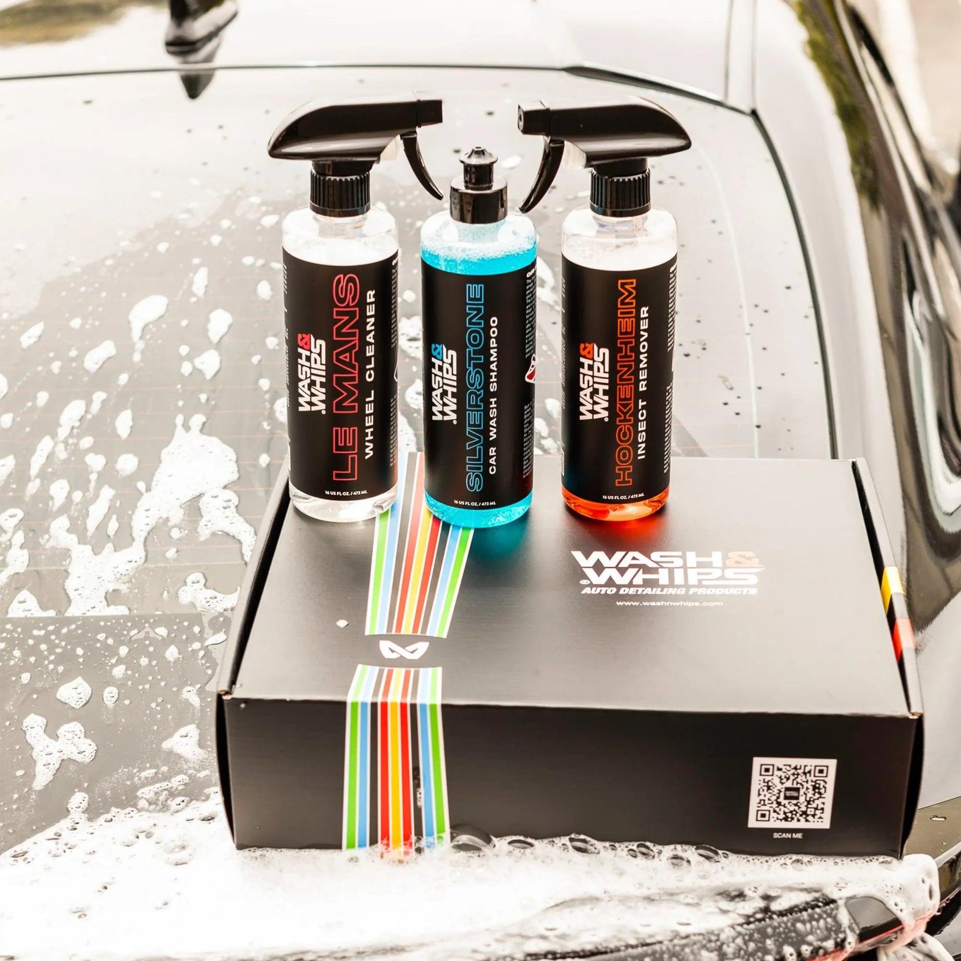 Car cleaning kit with wheel cleaner, car wash shampoo, and insect remover bottles on a foamy hood