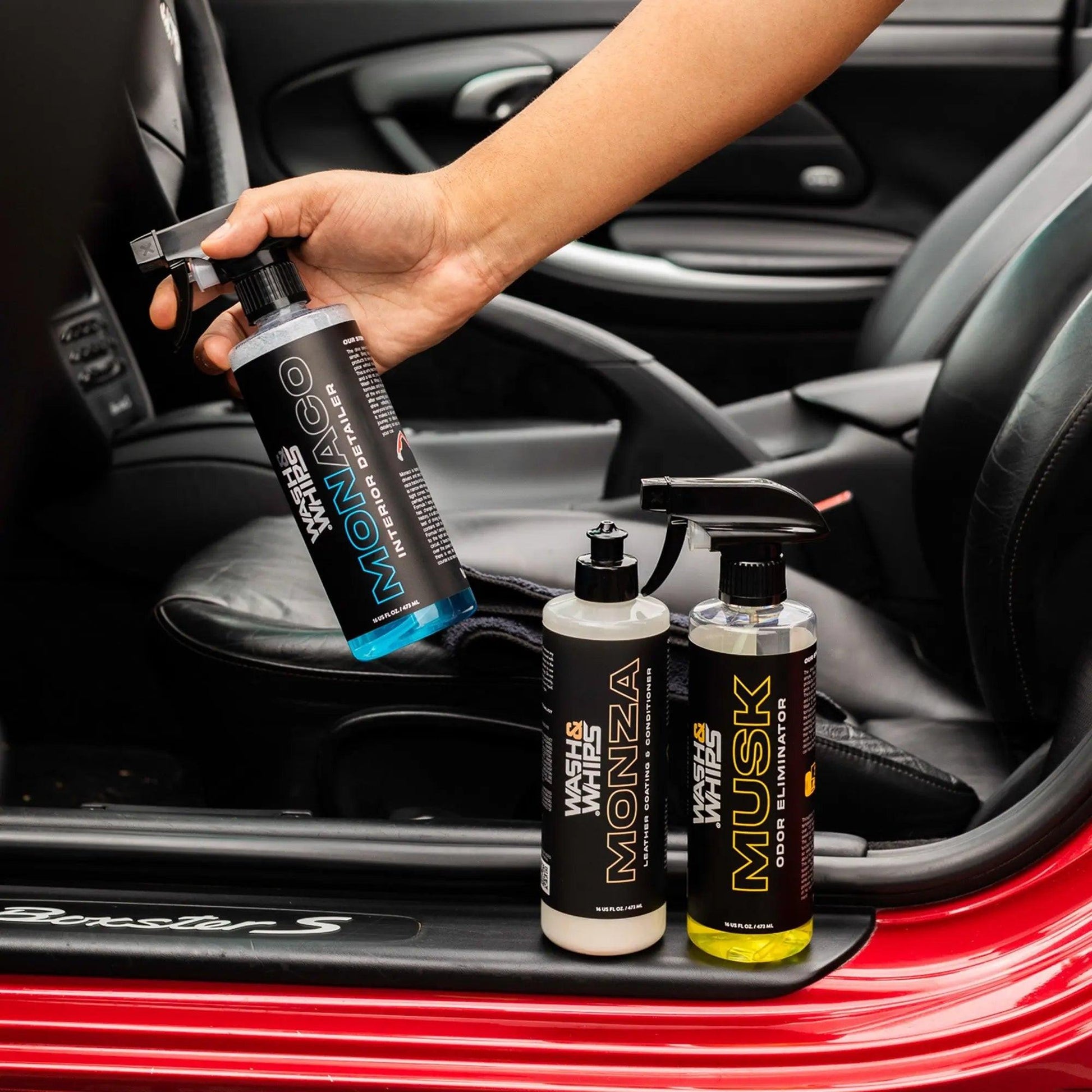 Hand holding Monza interior sealer bottle beside Monza and Musk car care products on car seat