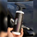Hand holding Wash & Whips Sonoma ceramic coating spray bottle in front of a car