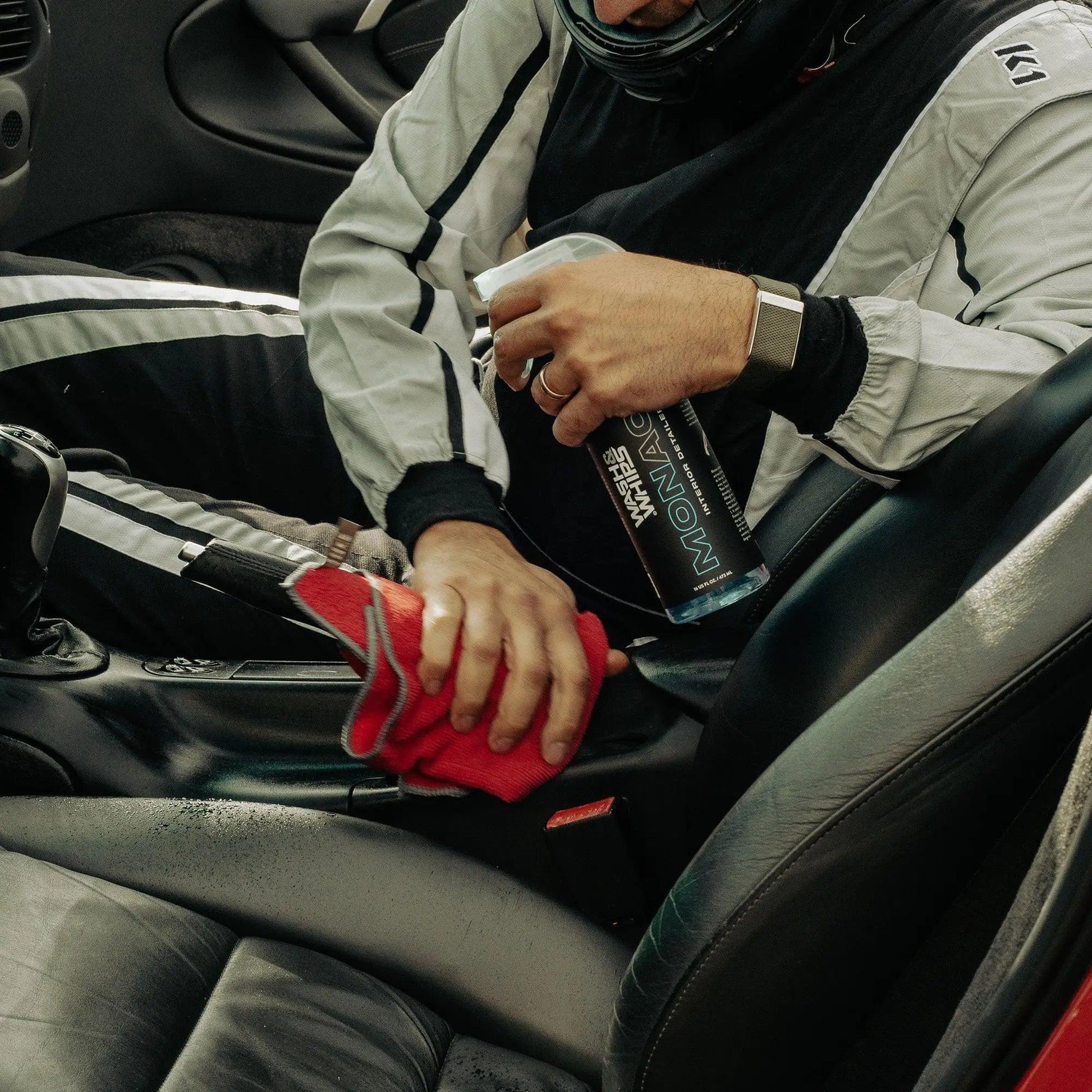 Man in racing suit cleaning car interior with spray bottle and red microfiber cloth
