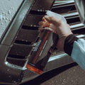 Hand holding Hockenheim insect remover spray near a wet car front grille, car cleaning product
