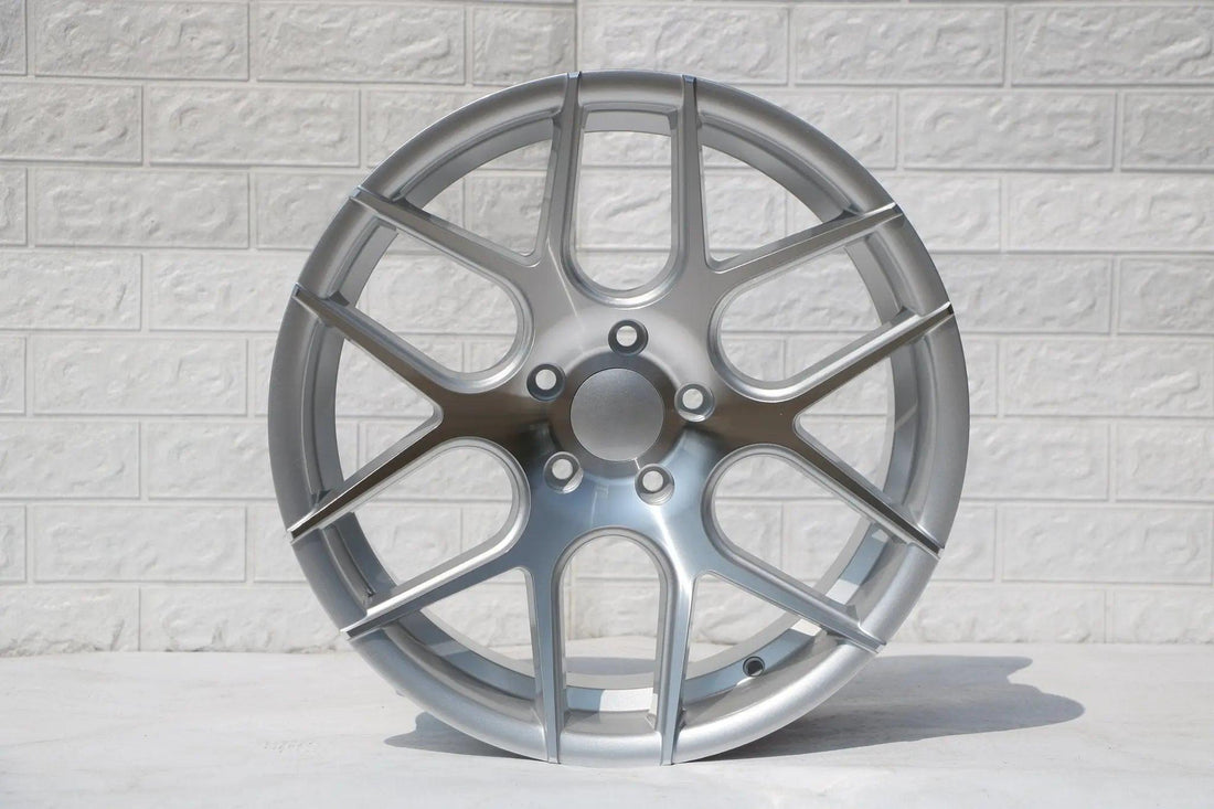 Silver multi-spoke alloy wheel with modern design against a light textured wall