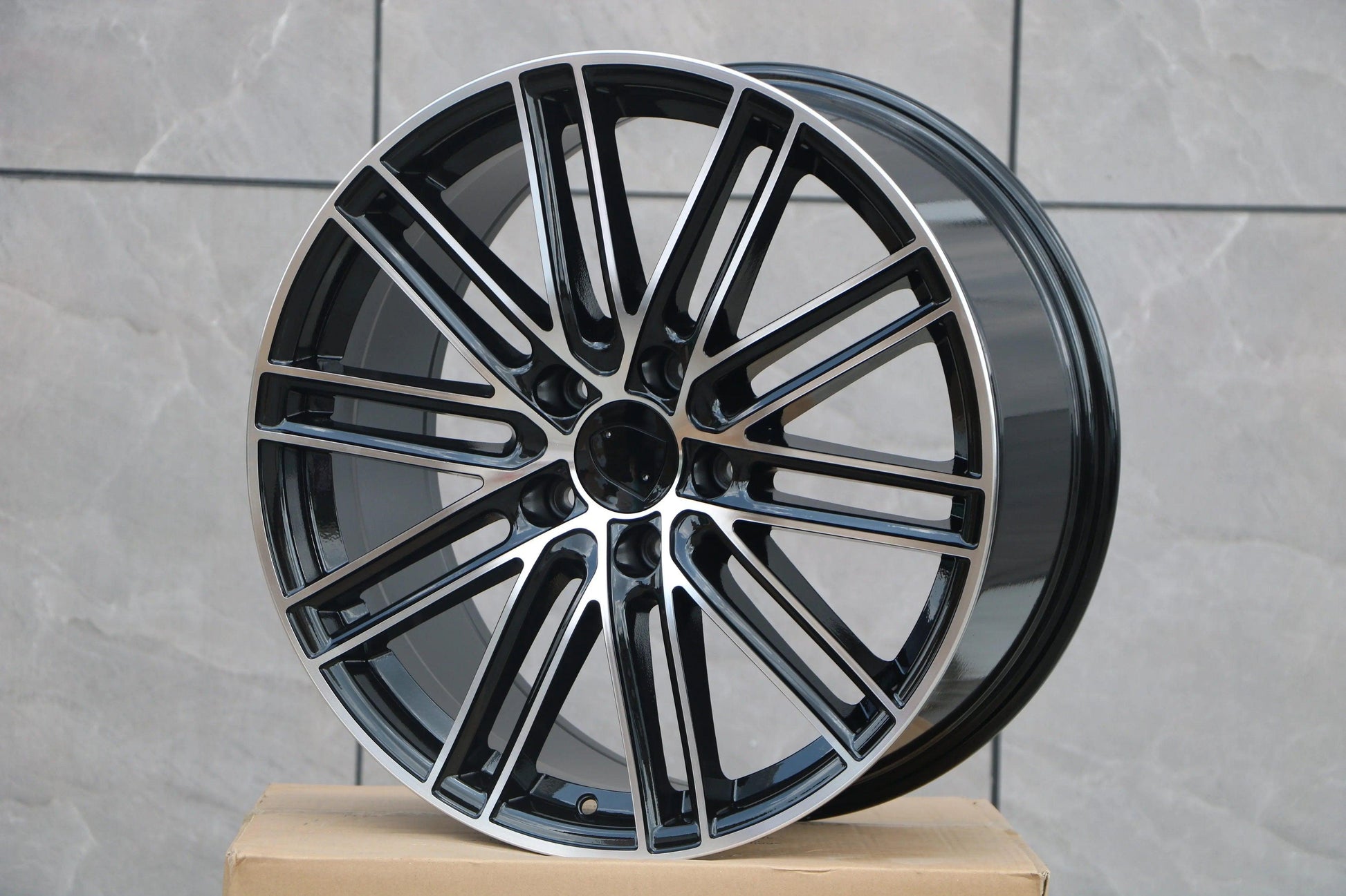 Gloss black and machined alloy wheel for Porsche Macan on a cardboard box, grey tile background