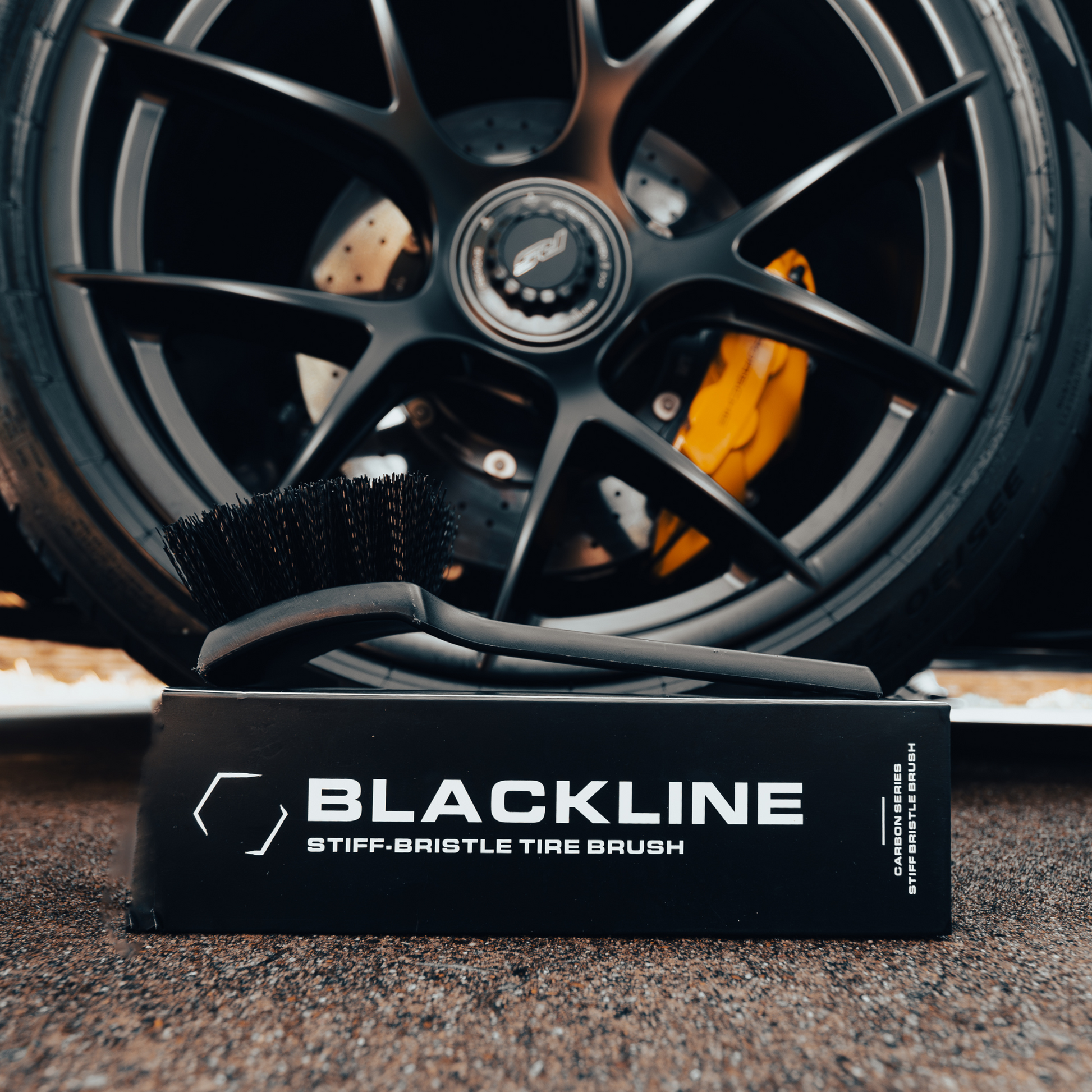 Blackline Car Care stiff bristle tire brush with durable handle for cleaning vehicle tires and wheels.
