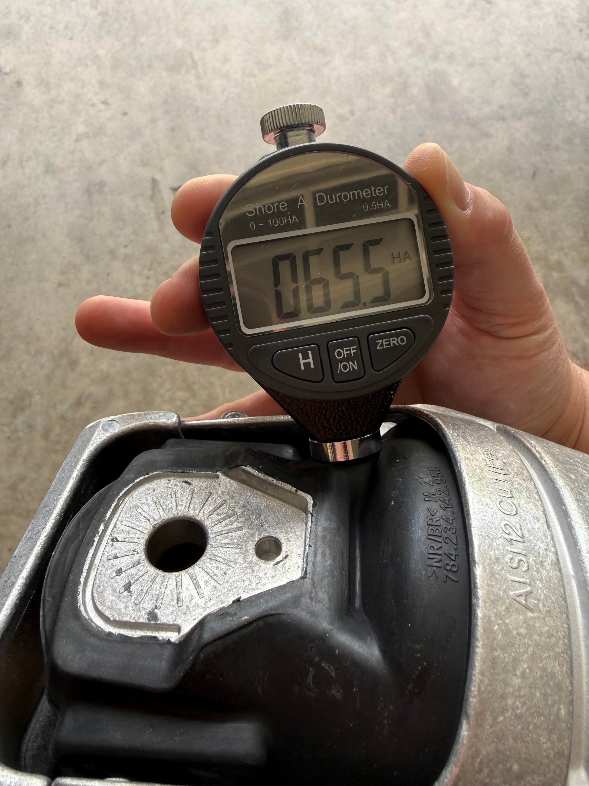 Digital durometer measuring hardness of automotive part, showing 65.5 HA for performance tuning.
