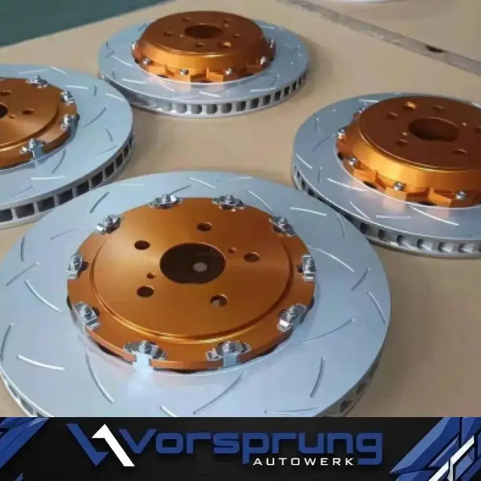 Slotted performance brake rotors with orange anodized centers on a workshop table.